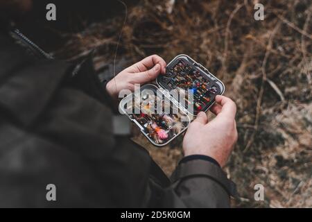 Pescatore che tiene la scatola dei lures di pesca del mosca nelle mani. Foto Stock