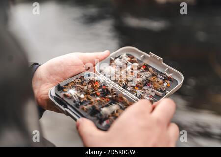 Pescatore che tiene la scatola dei lures di pesca del mosca nelle mani. Foto Stock