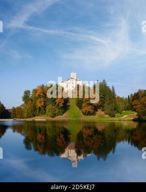 Castello Trakoscan in cima alla collina, riflesso del castello e cielo blu nel lago, autunno fogliame Foto Stock