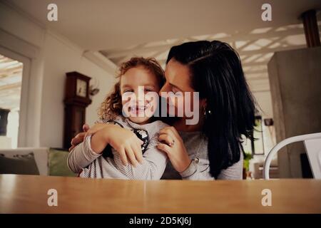 Ritratto di mamma allegra che solletico e baciante figlia seduta sedia a casa Foto Stock