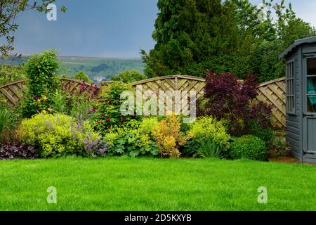 Giardino privato paesaggistico e soleggiato (design contemporaneo, fiori di confine estivi, fogliame colorato, capanna, prato, recinzione alta) - West Yorkshire, Inghilterra, Regno Unito. Foto Stock