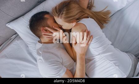 Felice giovane coppia coccolandosi insieme nel letto, giovane donna è incinta e partner amorevole tocca e carezza il suo vently teneramente, loro bacio. In alto Foto Stock