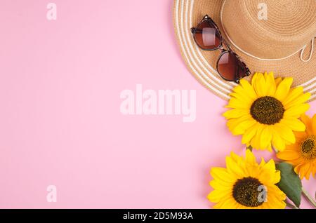 Flatlay con occhiali da sole, cappello di paglia e girasole giallo brillante su sfondo rosa Foto Stock