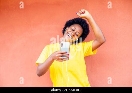 Foto autentica di un giovane millennial nero africano che si diverte utilizzo del telefono cellulare per l'ascolto di musica online Foto Stock