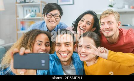 A casa diversi Gruppo di amici facendo collettivo Selfie, Guy tiene persone smartphone sorriso, ridere e fare anatra Lips.Young persone facendo Live Stream di Foto Stock