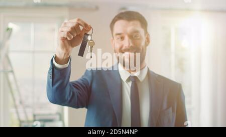 Agente immobiliare di successo in una tuta sorride e offre le chiavi da un nuovo appartamento. Spaziosa Nuova casa in vendita da Professional Real Estate Broker Foto Stock