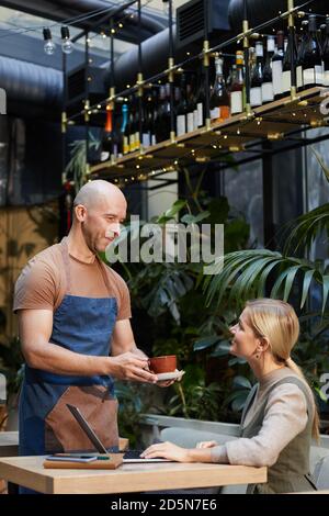 Giovane donna che ordina la tazza di caffè al cameriere mentre si siede al ristorante Foto Stock