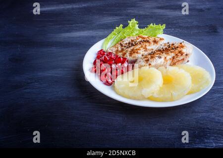 Filetti di pollo fritti con lattuga, ananas e semi di melograno su sfondo di legno nero, spazio copia, vista dall'alto. Foto Stock