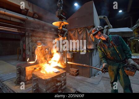 I lavoratori in un getto di fonderia di un pezzo di metallo - Sicurezza sul lavoro e il lavoro di squadra Foto Stock