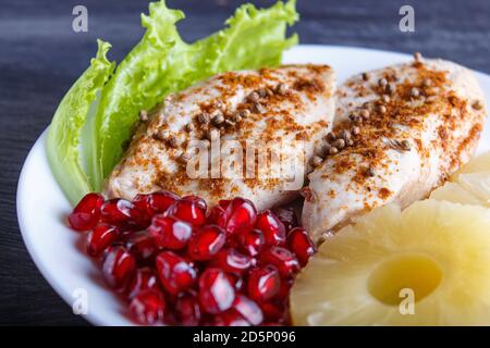 Filetti di pollo fritti con lattuga, ananas e semi di melograno su fondo di legno nero, spazio copia, primo piano. Foto Stock