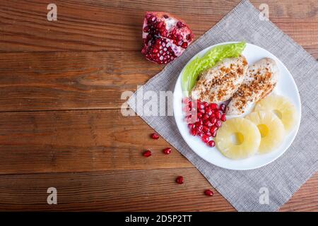 Filetti di pollo fritti con lattuga, ananas e semi di melograno su sfondo di legno marrone, spazio copia, vista dall'alto. Foto Stock