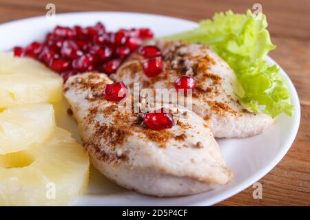 Filetti di pollo fritti con lattuga, ananas e semi di melograno su fondo di legno marrone, primo piano. Foto Stock