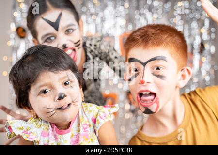 Gruppo di bambini in costumi di Halloween gesticulating e fare facce spaventose o spooky su sfondo decorato guardando in macchina fotografica. Foto Stock