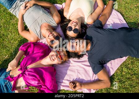 Un felice gruppo multietnico di amici che si riuniscono nel parco in una calda giornata estiva. Foto Stock