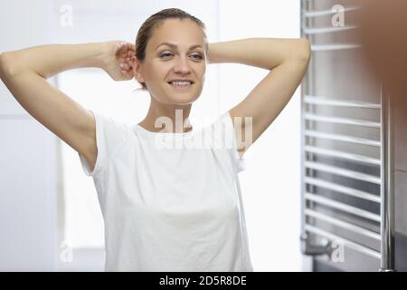 Donna in T-shirt bianca si erge di fronte allo specchio del bagno e sorride. Foto Stock