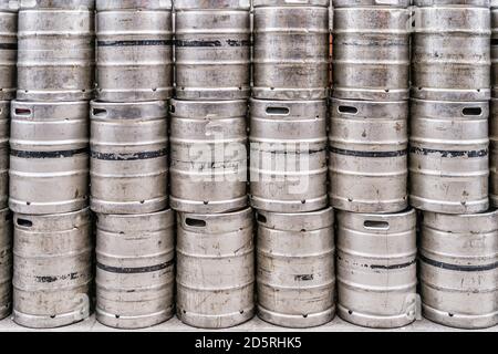 Parete di barili o barili di birra in acciaio inossidabile usati e graffiati. Impilati in una fila grandi barili o contenitori di colore argento o metallico Foto Stock