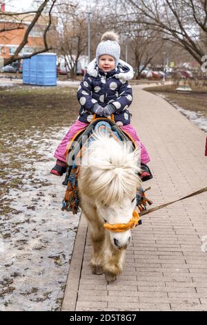 bambina che cavalca un pony in un parco invernale Foto Stock