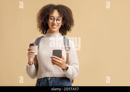 Dispositivi moderni per la comunicazione in remoto. Donna afroamericana sorridente in occhiali con zaino Foto Stock