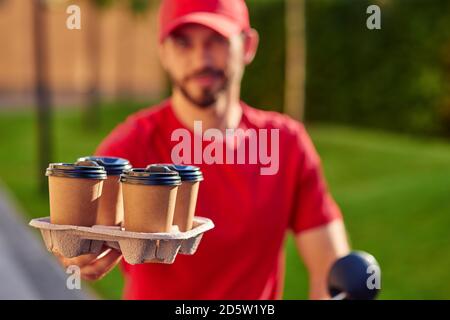 Tazze di caffè in piedi sulla tavola di consegna in mano del corriere dell'uomo all'aperto. Messa a fuoco selettiva. Concetto di consegna degli alimenti Foto Stock