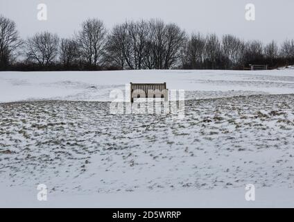Una panchina di parco su una collina innevata Foto Stock