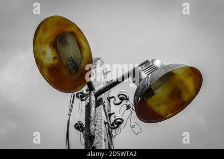 Vecchia lampada elettrica in metallo arrugginito su lampione in cemento - immagine in bianco e nero con colore selezionato e luce di copia Foto Stock