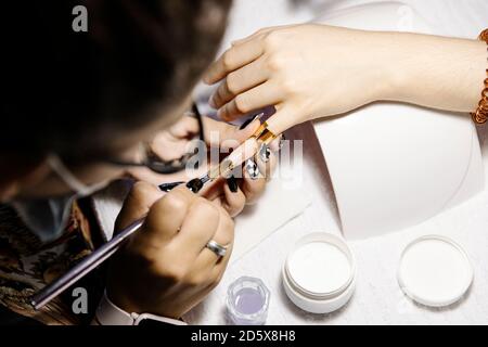 Da sopra stilista applicando vernice sulla punta del chiodo di coltivare la cliente femminile in salone Foto Stock