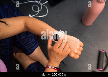 Primo piano donna che usa l'orologio intelligente dopo aver fatto esercizio a casa. Concetto di tecnologia sportiva per il controllo dei dati sanitari. Foto Stock