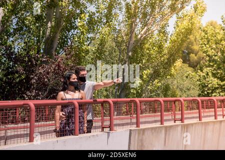 Giovane uomo che punta con la mano con la sua ragazza indossando maschera facciale per prevenire il virus. Foto Stock
