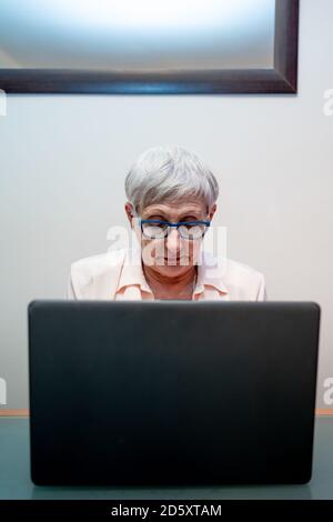 Caucasica donna anziana capelli bianchi e occhiali blu con un computer portatile Foto Stock