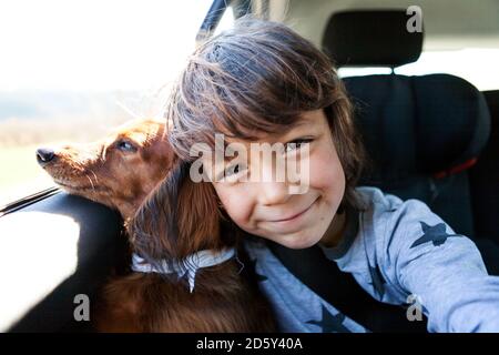 Ritratto del ragazzino sorridente seduto con il suo dachshund dai capelli lunghi in auto Foto Stock