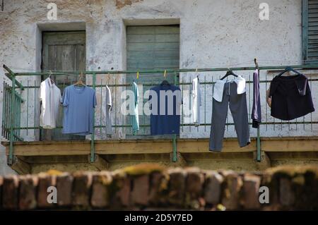 sfumature di vestiti blu che asciugano al sole appeso sopra filo in primo piano e la vecchia facciata della casa sullo sfondo Italia Foto Stock