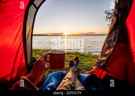 Uomo in campeggio in Estonia, guardando il tramonto sdraiato in tenda Foto Stock