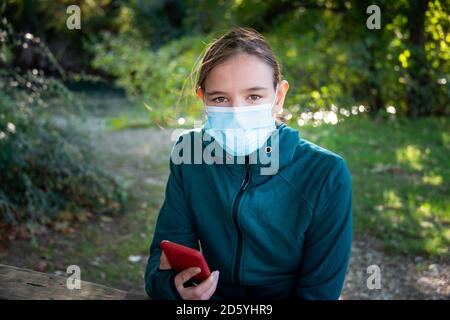 giovane donna fuori in campagna con una maschera che tiene un telefono cellulare . Foto Stock