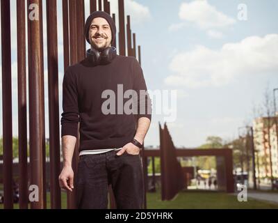 Ritratto di sorridente giovane con le cuffie da indossare cappello di lana e la maglia nera Foto Stock