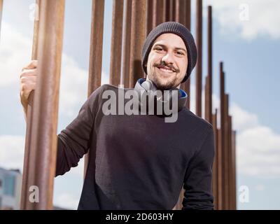 Ritratto di sorridente giovane con le cuffie da indossare cappello di lana e la maglia nera Foto Stock