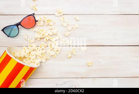 Anteprima concept del film. Il popcorn fuoriesce dalla scatola e dagli occhiali 3D. Sfondo in legno chiaro, spazio libero per il testo, vista dall'alto. Foto Stock