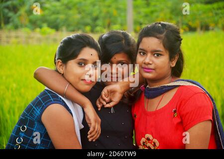 Primo piano di tre ragazze adolescenti che indossano abiti colorati tradizionali indiani sorridenti in un campo di risaie del Bengala Occidentale, focalizzazione selettiva Foto Stock