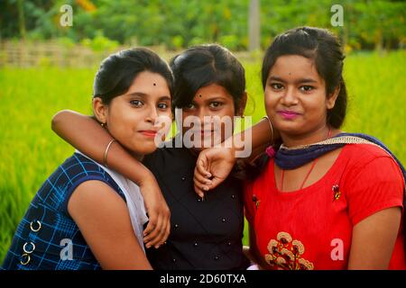 Primo piano di tre ragazze adolescenti che indossano abiti colorati tradizionali indiani sorridenti in un campo di risaie del Bengala Occidentale, focalizzazione selettiva Foto Stock