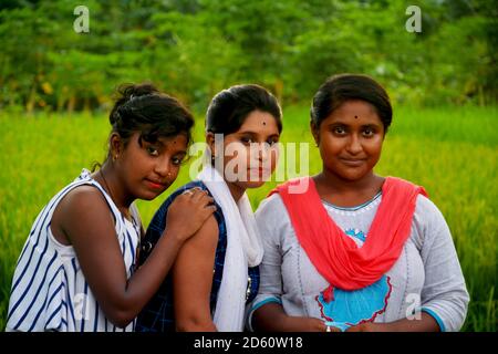 Primo piano di tre ragazze adolescenti che indossano abiti colorati tradizionali indiani sorridenti in un campo di risaie del Bengala Occidentale, focalizzazione selettiva Foto Stock