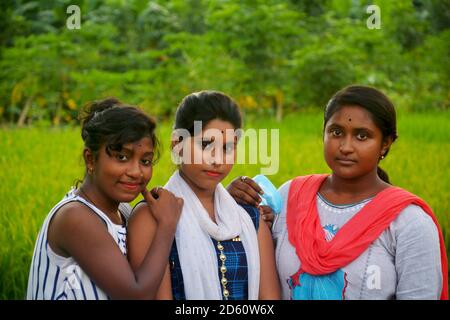 Primo piano di tre ragazze adolescenti che indossano abiti colorati tradizionali indiani sorridenti in un campo di risaie del Bengala Occidentale, focalizzazione selettiva Foto Stock