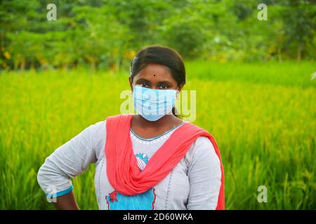 Primo piano di una ragazza teenage che indossa una maschera e si trova in un campo agricolo con risone verde, messa a fuoco selettiva Foto Stock