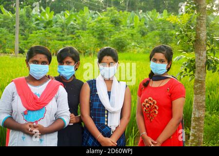 Primo piano di quattro ragazze adolescenti che indossano la maschera facciale in piedi in un campo di risaie agricolo, messa a fuoco selettiva Foto Stock