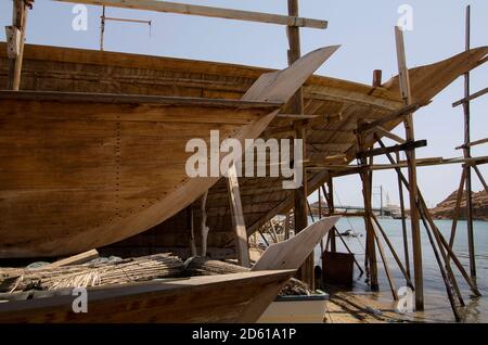 Una vista del tradizionale dhow cantiere di costruzione in legno al porto di sur sulla costa di OmanOman ha una lunga e ricca storia marittima e la città portuale di sur continua l'eredità. Il sambuco arabo è una tradizionale nave a vela in legno, realizzata a mano da artigiani che utilizzano tecniche antiche del secolo. Fatto su ordinazione le barche sono più probabili essere impiegate nel settore del turismo di quello del commercio marittimo che ha dato al porto la sua preminenza. Foto Stock