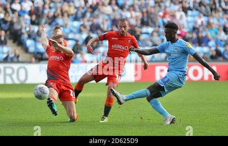 Jordy Hiwula di Coventry City (a destra) ha un colpo sul gol, sotto la pressione di Jason McCarthy di Wycombe Wanderers (a sinistra) e Michael Harriman Foto Stock