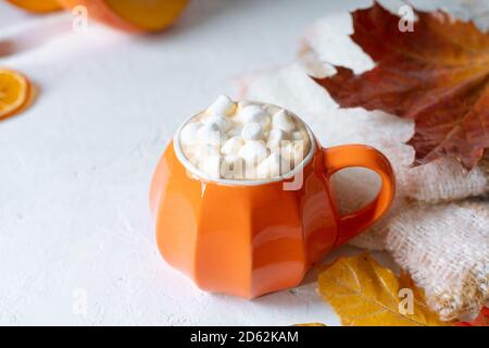 Composizione con tazza di caffè in stile zucca arancione con marshmallows e decorazioni a tema autunnale, foglie cadute, maglione accogliente su sfondo bianco. Foto Stock