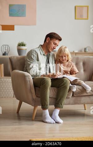 Padre disegnando un'immagine nel blocco note con il suo piccolo figlio che imparano a tirarlo seduto sul divano dentro la camera Foto Stock