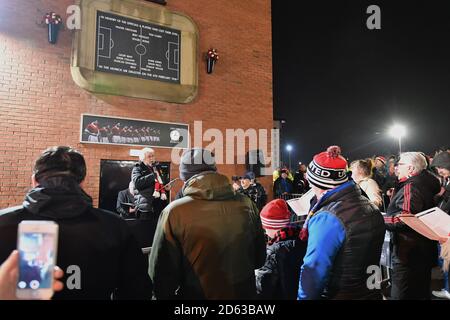 Pete Martin canta i Fiori di Manchester come tifosi di calcio Ascolta un servizio memoriale per commemorare l'aereo di Monaco Crash sotto l'orologio di Monaco fuori Old Trafford Foto Stock