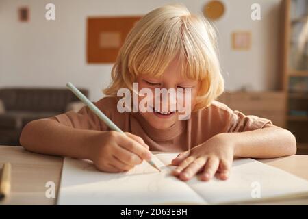 Bambino con i capelli biondi che scrive il rapporto nel libro di nota fa i compiti dopo la scuola Foto Stock