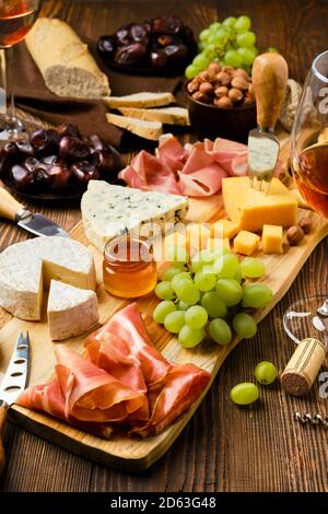 Piatto di formaggi con prosciutto, uva, miele, datteri, cracker, noci e vino su fondo ligneo con spazio per la copia Foto Stock