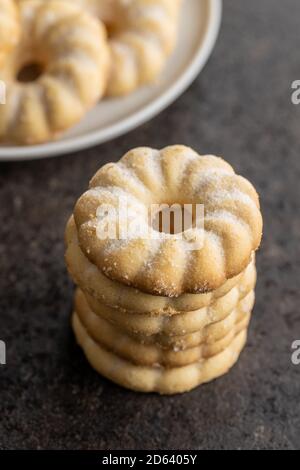 Dolci anelli biscotti. Biscotti al gusto di vaniglia cosparsi di zucchero su tavola nera. Foto Stock